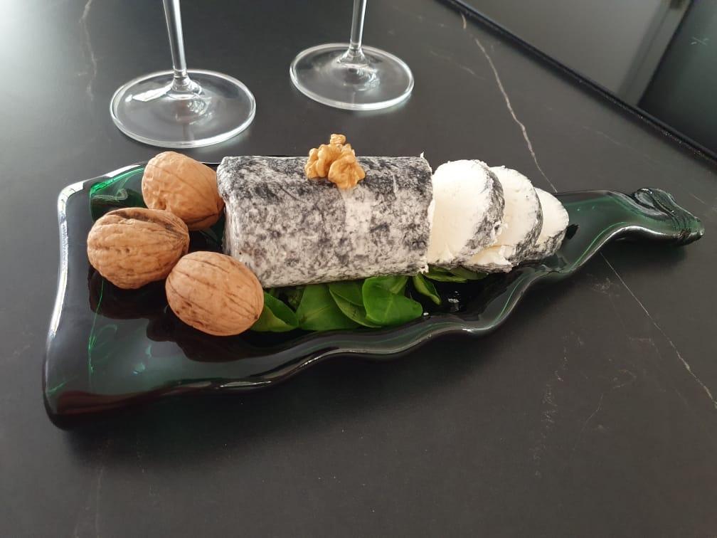 Une bouteille de vin déformée qui est une planchette apéritive et à fromage avec du fromage de chèvre et des noix .