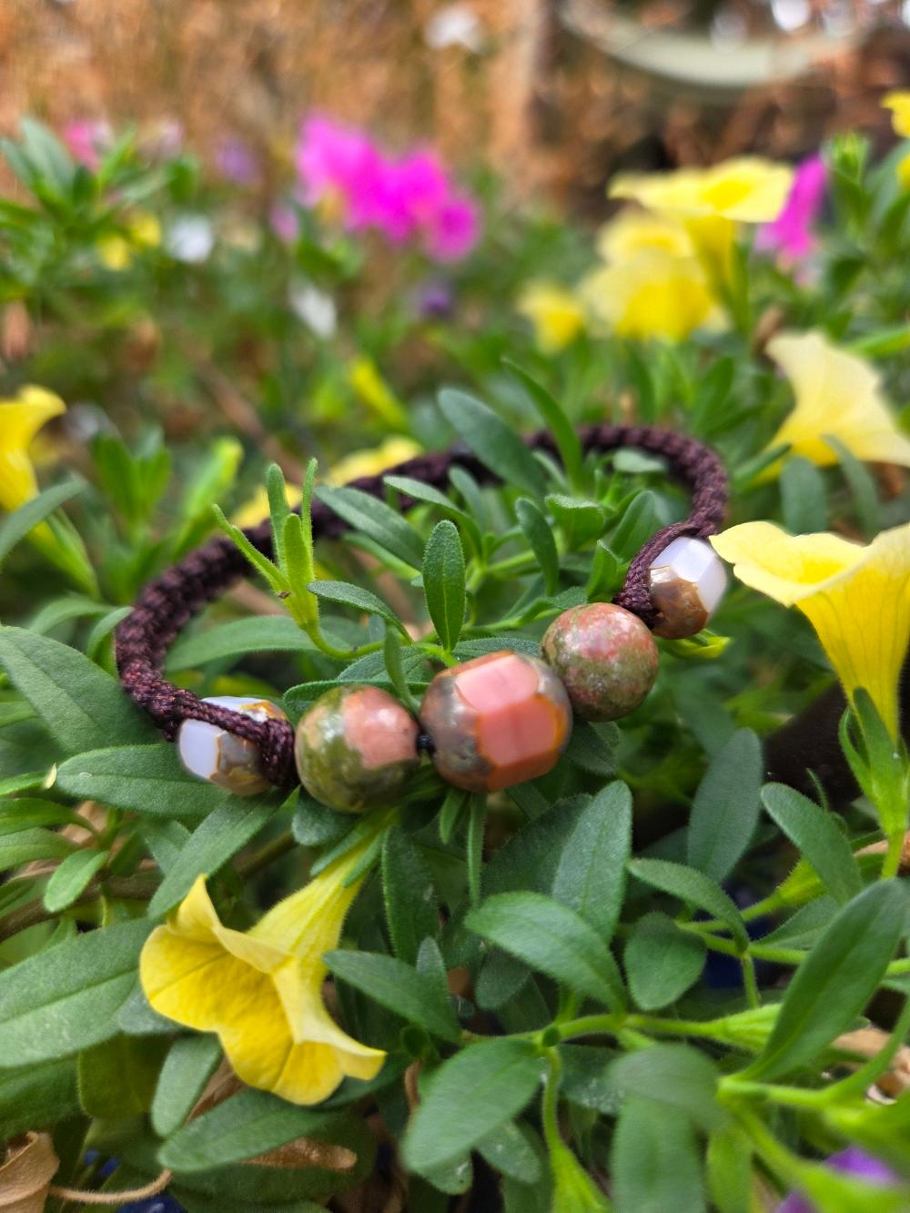 Un bracelet tréssé avec des perles en pierres naturelles et de verre posé sur des fleurs jaunes .D'Ici et de Claire 