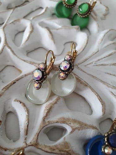 Boucles d'oreilles pendantes rondes avec pierres scintillantes sur un fond blanc. Nathalie Borderie