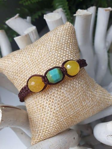 Bracelet artisanal avec perles jaunes et turquoise sur un coussin beige.