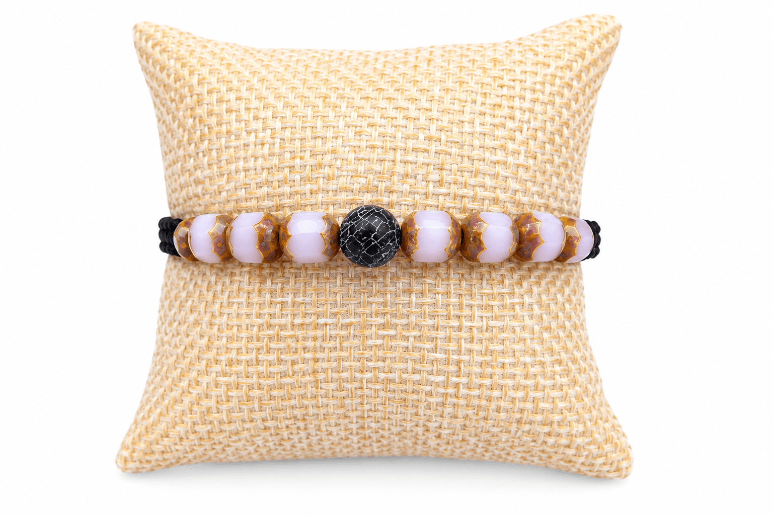 Coussin beige avec autour un bracelet tréssé , perles roses et noires ; D'Ici et de Claire 