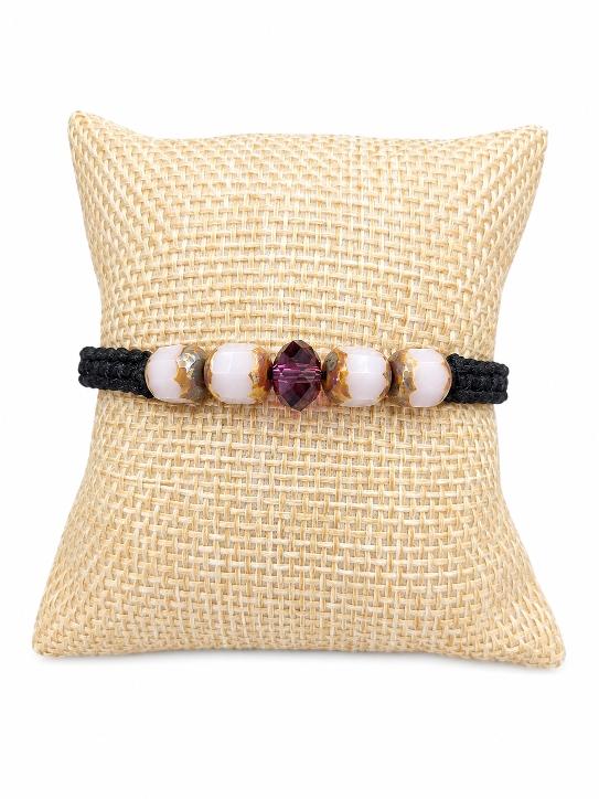 Un bracelet tréssé sur un coussin beige , le bracelet comporte des perles en verre et une perle en cristal autrichien rose .Création originale de D'Ici et de Claire 