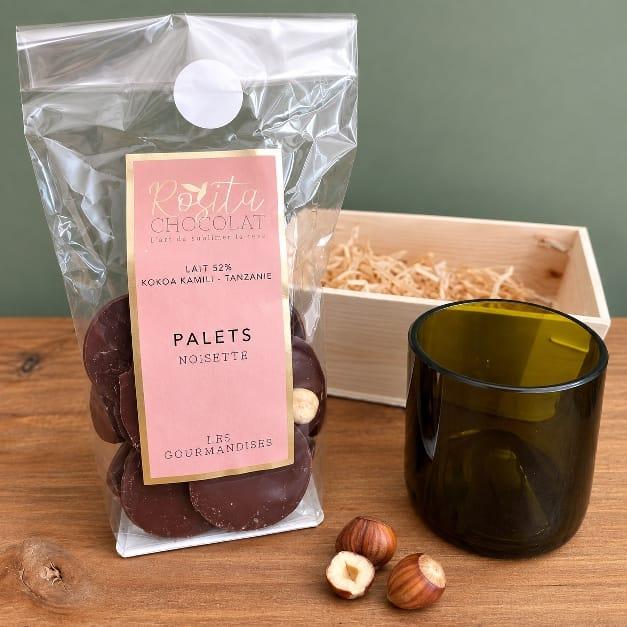 un sachet de palets de chocolat à la noisette de chez rosita chocolat , une tasse à café et une mini cagette en bois 