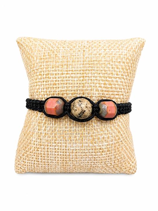 Un bracelet tréssé avec deux perles roses en verre et une perle en pierre naturelle de Syénite , posé sur un coussin beige ; D'Ici et de Claire