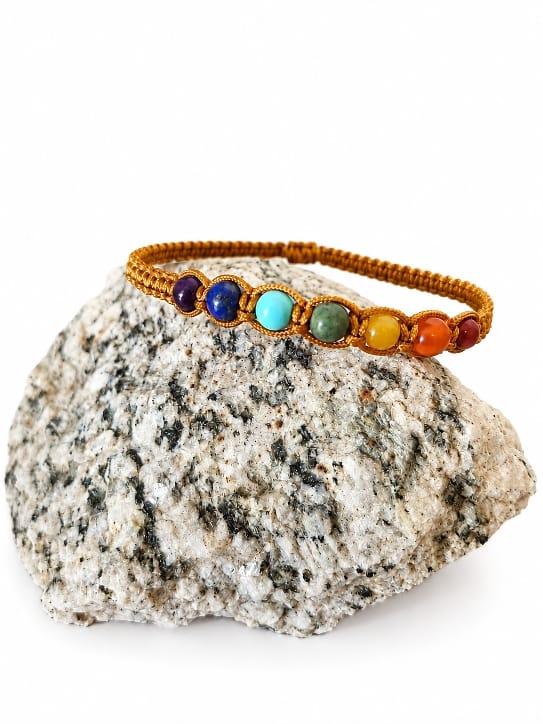 Bracelet avec des perles en pierres naturelles des couleurs des 7 chakras , posé sur une pierre .D'Ici et de claire 