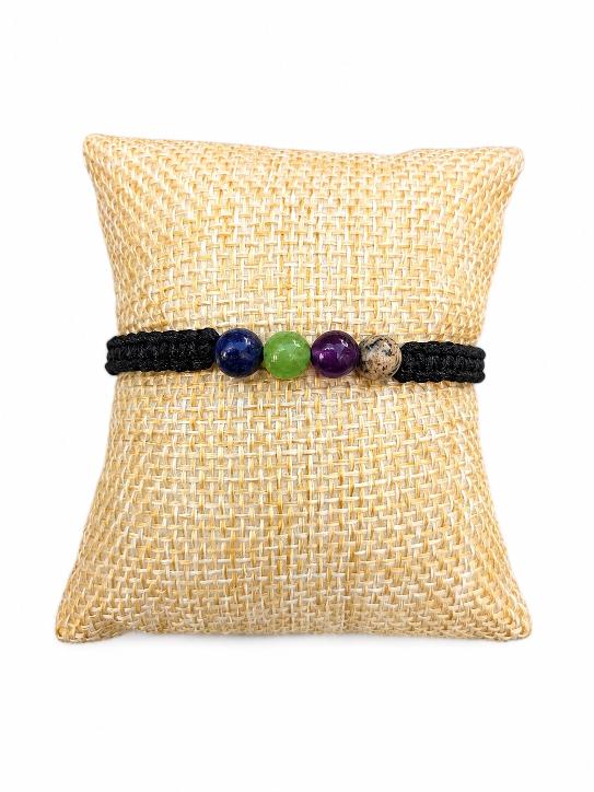 Un bracelet tréssé avec des perles en pierres de différentes couleurs sur un coussin marron clair.D'Ici et de Claire
