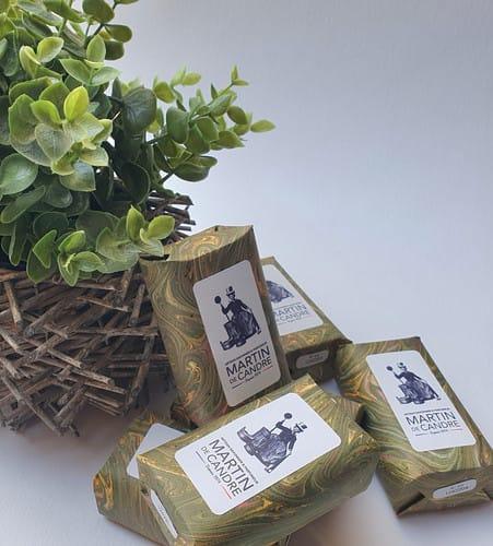 Plusieurs savons emballés avec étiquettes, près d'une plante verte. D'Ici et de Claire
